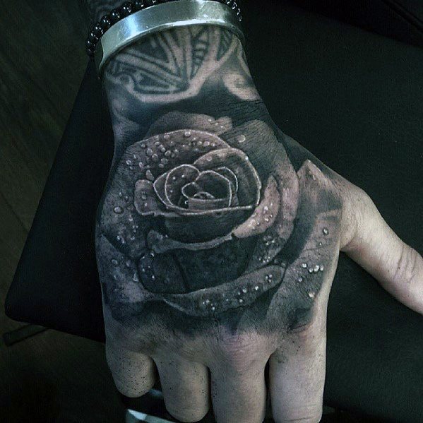 A stunning close-up of a lifelike rose tattoo graces the person's hand, with delicate water droplets enhancing its realism