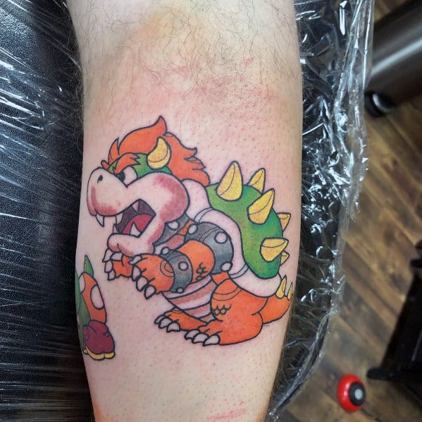 Cartoon-style Bowser tattoo on a man's forearm featuring bold outlines, vibrant colors, and a playful pose with a classic Mario-inspired design.