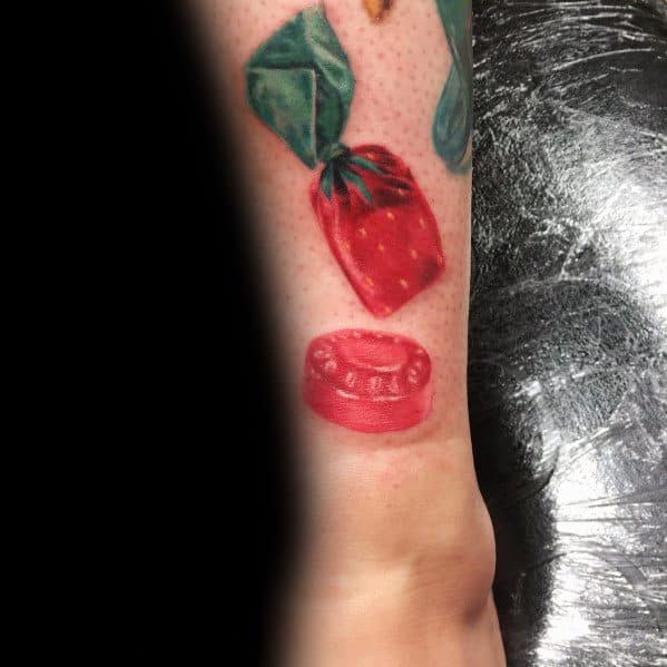 Realistic strawberry candy tattoo featuring an unwrapped piece and its wrapper, with detailed shading and highlights for a lifelike 3D effect.