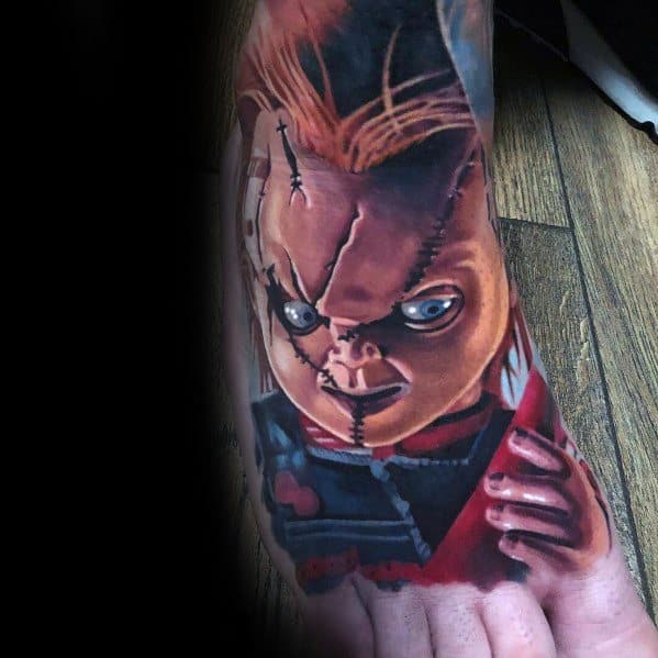Realistic Chucky foot tattoo with intense shading, featuring his stitched face, piercing blue eyes, and a bloodied weapon for a bold horror design.