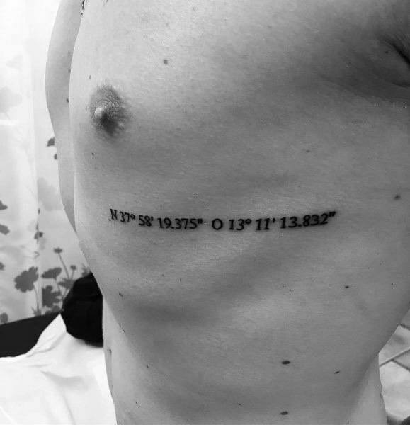 Minimalist coordinate tattoo on the ribcage with clean black lettering, marking a significant location with a sleek and subtle design.
