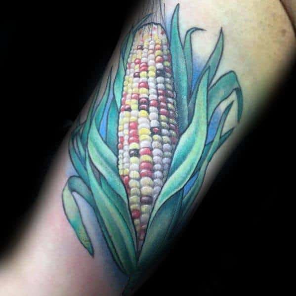 Vibrant tattoo of a multicolored corn cob with lush green husks, featuring detailed shading and realistic texture.