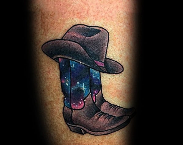 Tattoo of cowboy boots with a hat, featuring a cosmic galaxy design, blending Western tradition with a celestial and adventurous theme.