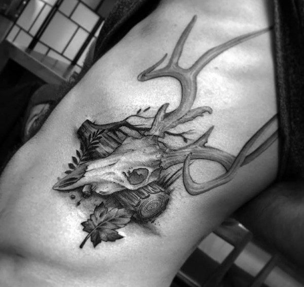 Realistic black and grey elk skull tattoo on the ribcage, featuring intricate antlers, forest elements, and fine shading for a bold, nature-inspired design.