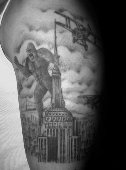 Empire State Building tattoo depicting King Kong atop the building, surrounded by planes, in detailed black-and-grey shading.