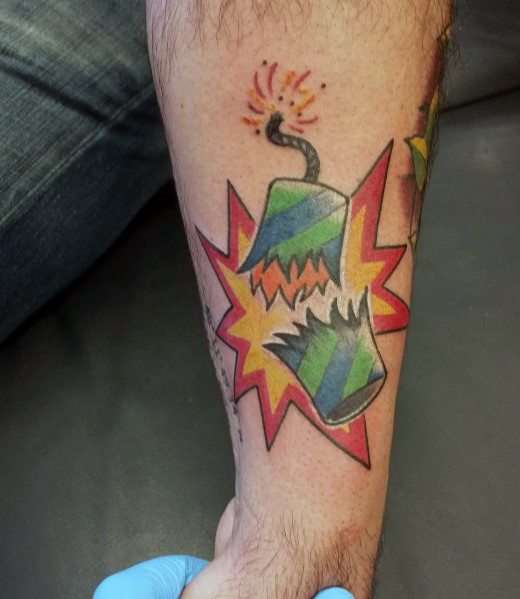 Tattoo of an exploding firecracker with a lit fuse, bursting apart in a bold comic-style design with bright colors and dynamic shading.