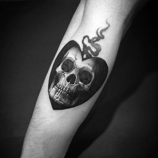 Black and grey forearm tattoo featuring a skull inside a heart shape with smoke rising, blending gothic and dark romantic elements.