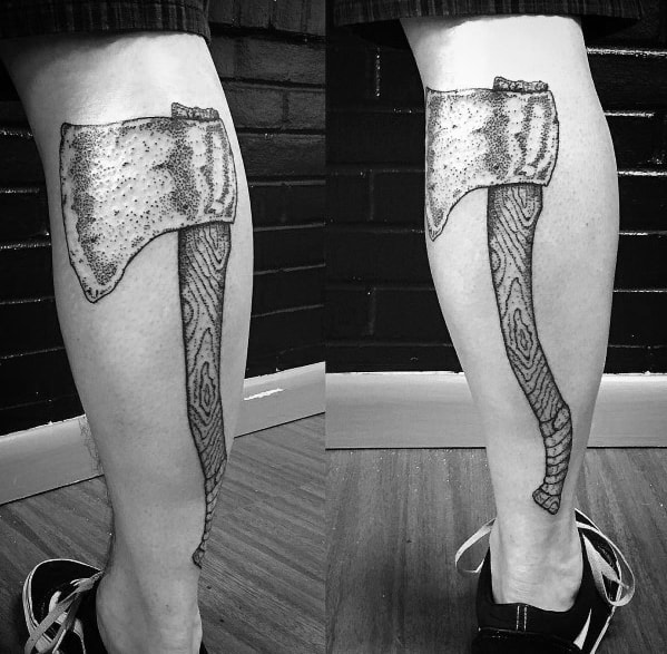 Large black and grey hatchet tattoo on the calf, featuring a wood-grain textured handle and a rugged, stippled blade for a bold, realistic look.