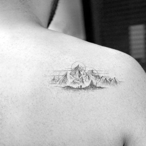 Small, detailed mountain tattoo on the upper back, featuring fine linework and a rising sun, symbolizing adventure and tranquility.