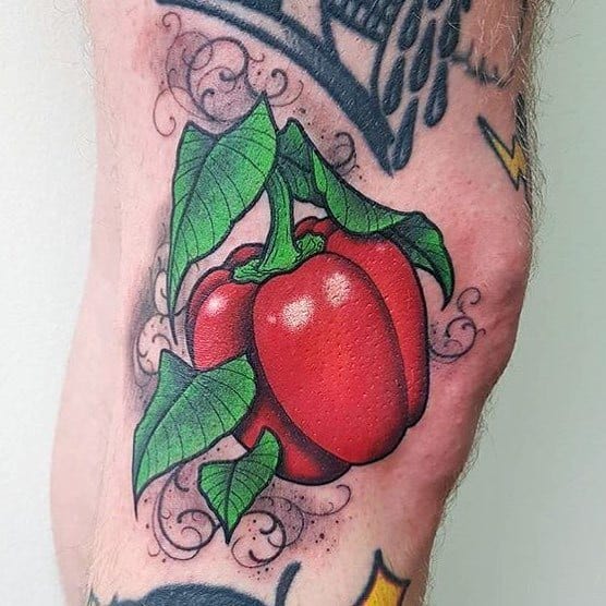 Vibrant red bell pepper tattoo with bold shading, green leaves, and decorative swirls, creating a dynamic and eye-catching design.