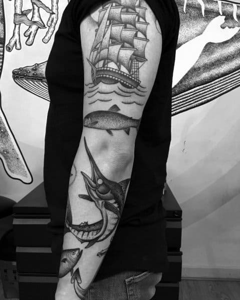 Black and grey nautical sleeve tattoo featuring a sailing ship, a salmon, and a marlin, combining maritime and aquatic elements in a bold design.