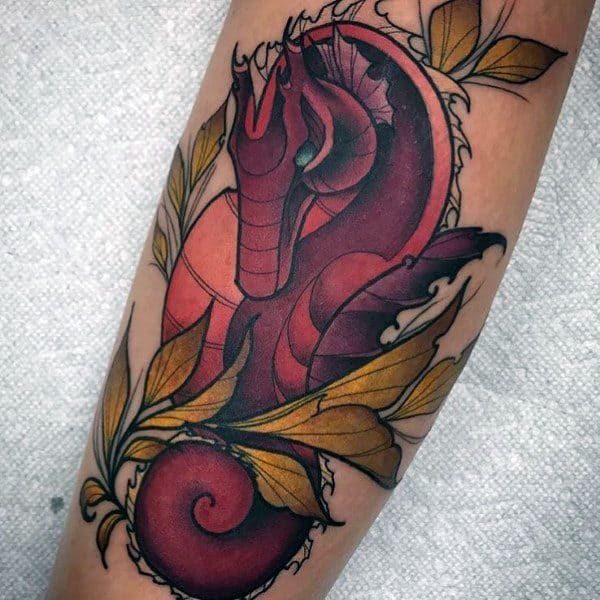 Neo-traditional seahorse tattoo on forearm, featuring bold red hues, intricate linework, and golden leaves for a striking and artistic design.