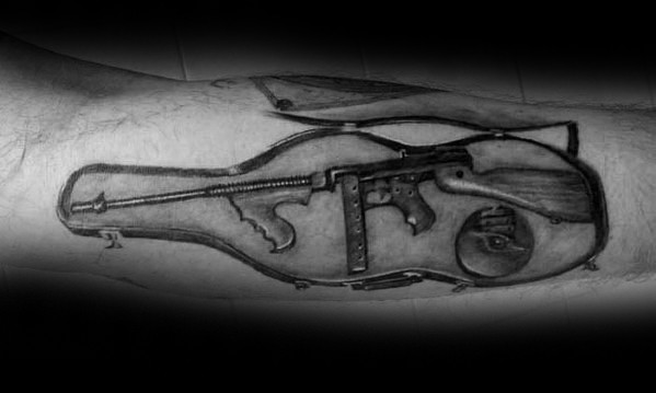Black and grey Tommy gun tattoo featuring the firearm inside an open violin case, symbolizing the classic gangster era with detailed shading and realism.