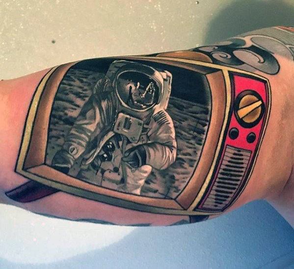 Tattoo of a vintage TV displaying a detailed black and grey astronaut on the moon, framed by bold red and gold dials, blending realism with nostalgia.