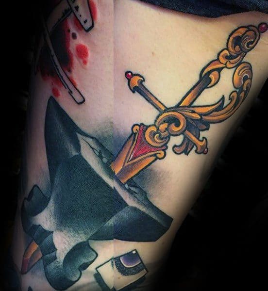 Vibrant anvil tattoo featuring a detailed ornate sword striking into it, with bold black shading and rich gold, red, and purple accents.