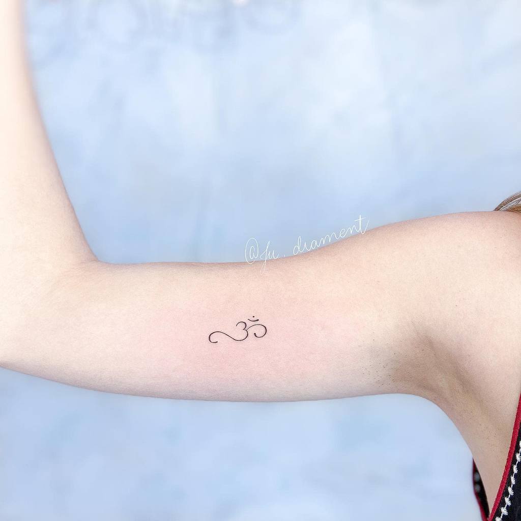 A minimalist "Om" tattoo graces a person's inner arm, subtly urging them to breathe