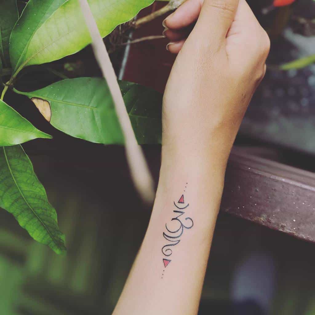 Minimalist Om symbol tattoo on the wrist with geometric accents and small pink triangles, inked in fine black lines