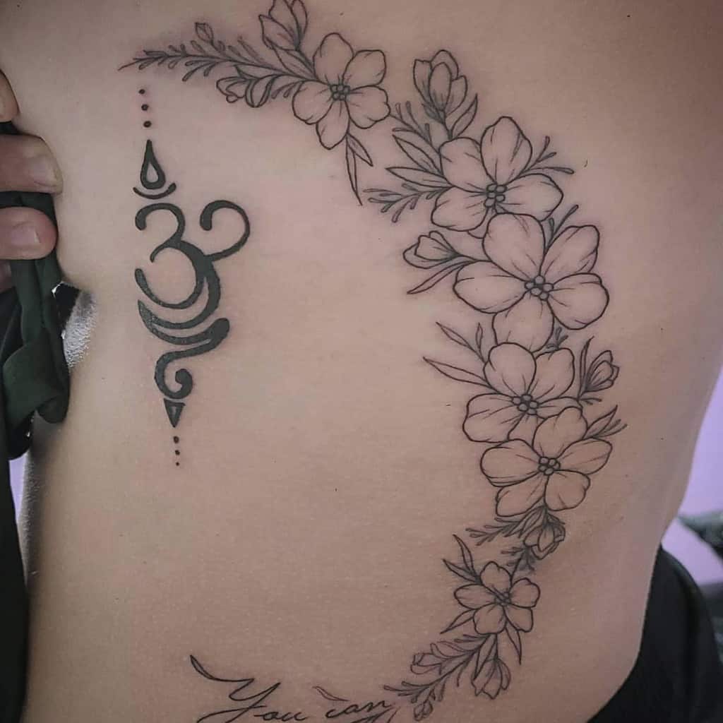 Side tattoo featuring a bold Om symbol paired with a delicate floral design of outlined flowers and leaves in black ink