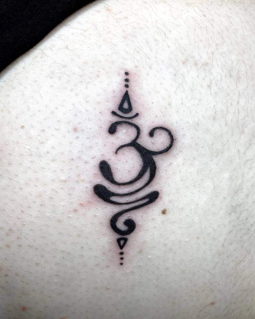 A black Om symbol tattoo with decorative lines graces the skin, whispering a reminder to breathe deeply