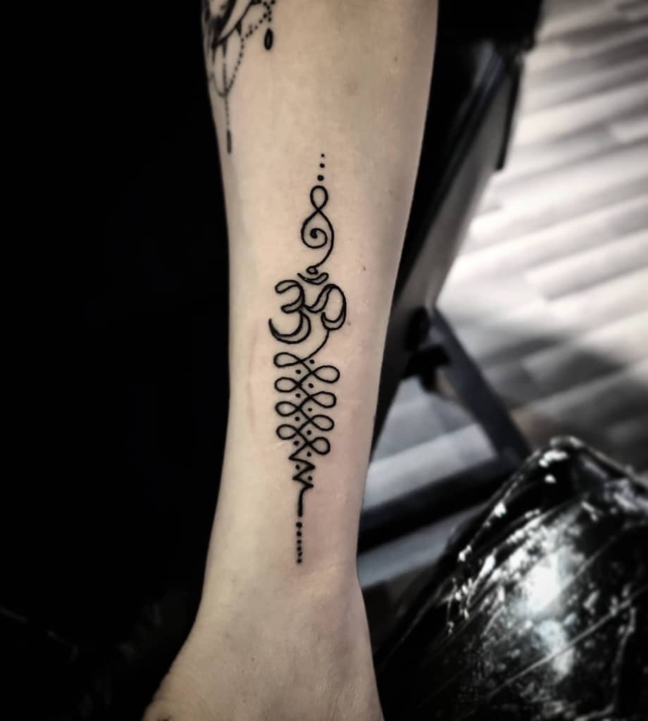 Forearm tattoo featuring a stylized Om symbol with flowing geometric patterns and dotted accents in bold black ink