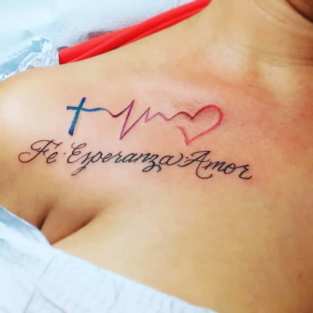 Tattoo on upper chest with a cross, heartbeat line, heart, and the words "Fe Esperanza Amor" in cursive