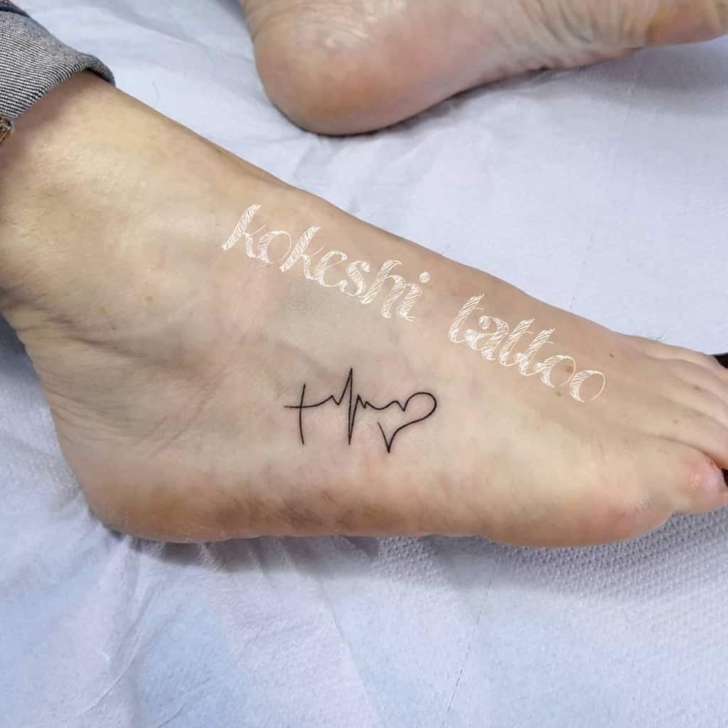 Small and simple foot tattoo of a cross, heartbeat line, and heart symbol in fine black ink