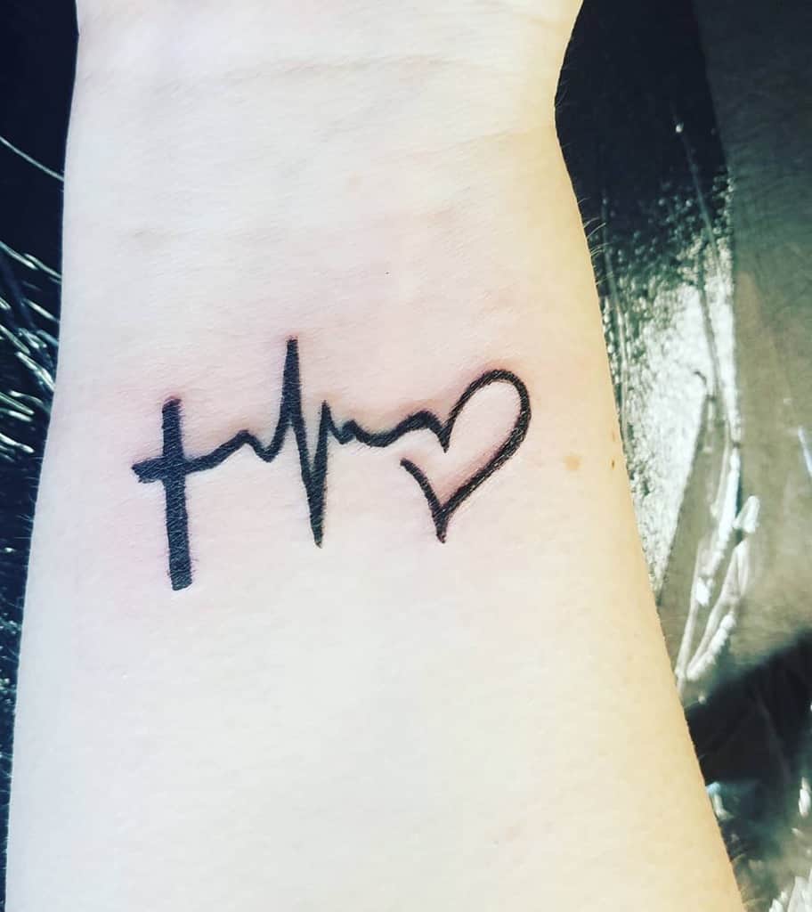 Tattoo of a cross, heartbeat line, and heart on a wrist