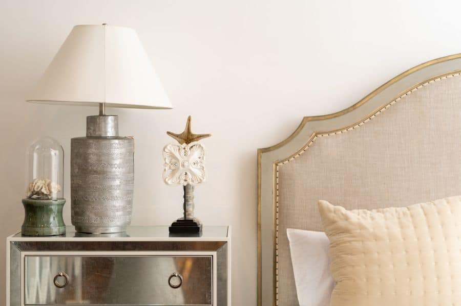Elegant bedside with silver lamp mirrored nightstand and upholstered headboard.