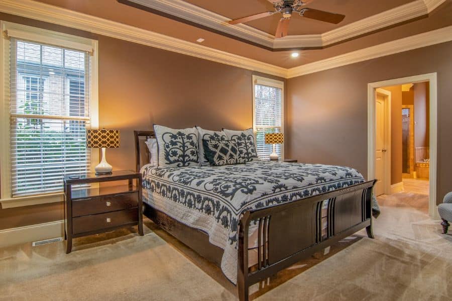 Traditional bedroom with wood bed patterned bedding tray ceiling and ceiling fan.
