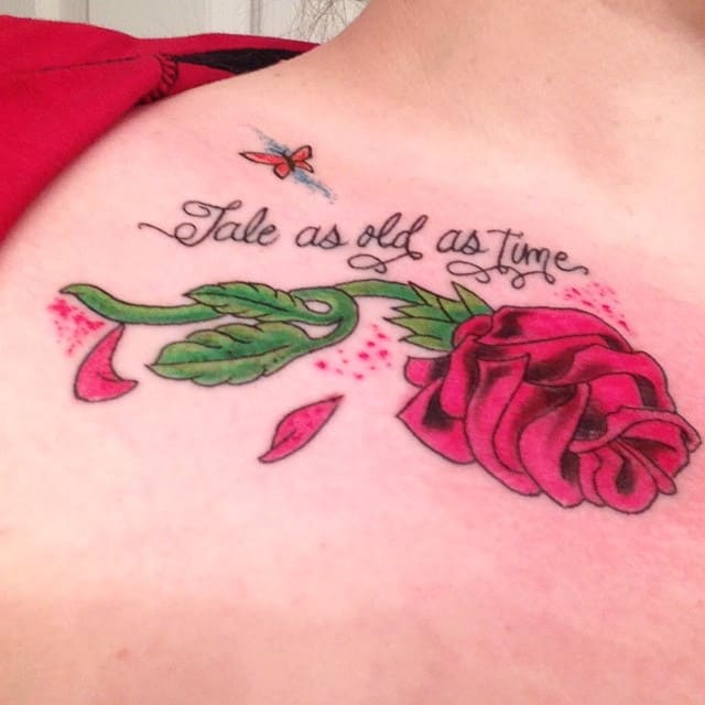 A tattoo on the shoulder featuring a vibrant red rose, green stem, a fluttering butterfly, and the quote "Tale as old as time"