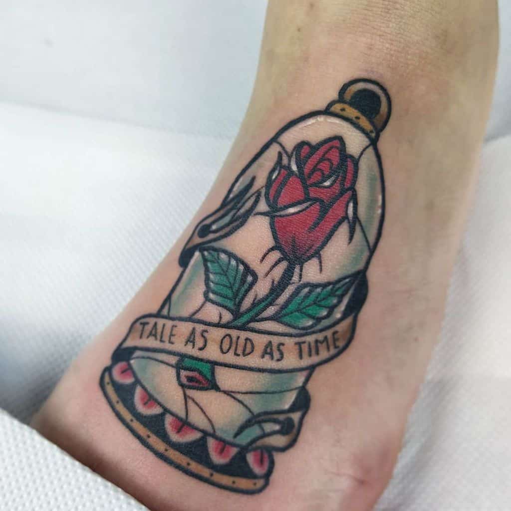 A tattoo of a red rose inside a glass dome with the quote "Tale as old as time" on a ribbon, featuring bold outlines and vibrant colors