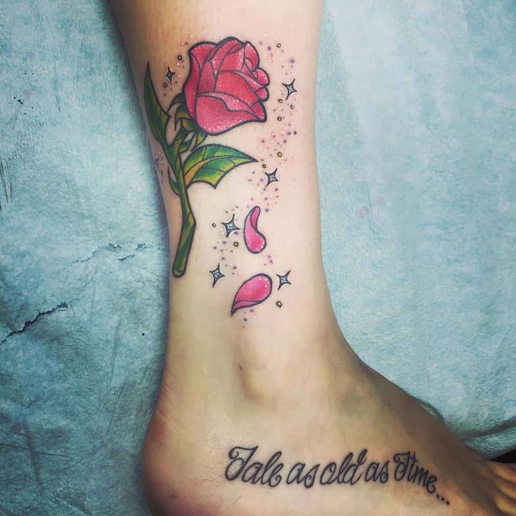 A tattoo of a pink rose with petals and sparkles, accompanied by the quote "Tale as old as time" beneath it