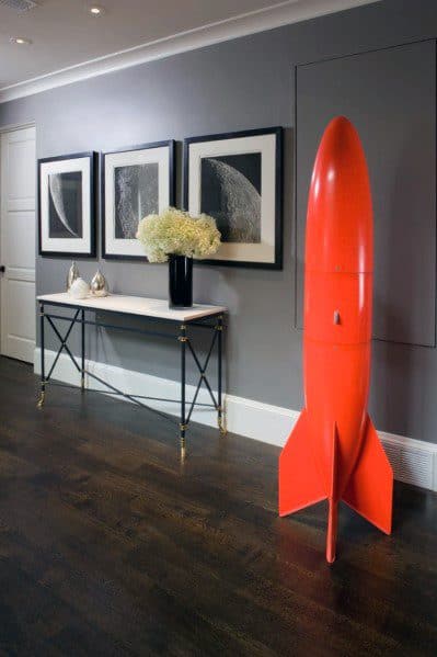 Modern hallway with gray walls, dark wood floors, and bold red rocket decor piece.
