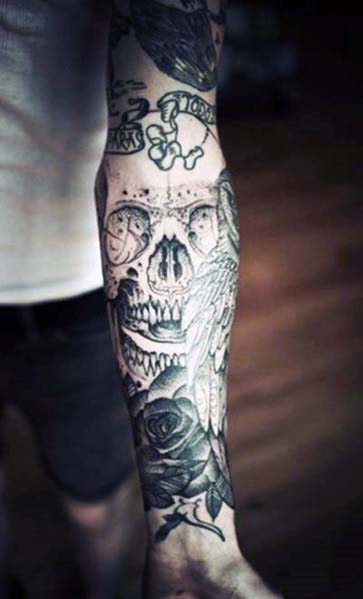 Close-up of a sleeve tattoo on an arm, intricately detailed with a skull, wings, and a rose