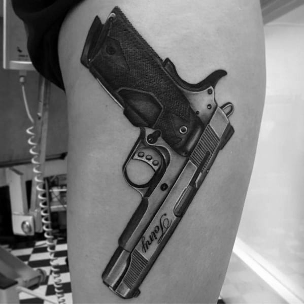 Realistic black and gray tattoo of a 1911 pistol on the thigh, featuring fine details, grip texture, and a custom engraving for a bold design.