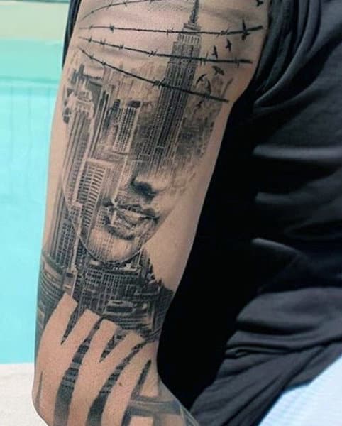 Tattoo on an arm featuring NYC skyline, a woman's face, and barbed wire with birds