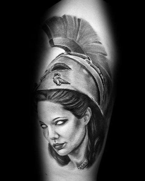 Athena tattoo with glowing white eyes, detailed plumed helmet, and soft black and grey shading on the upper arm for a mystical look