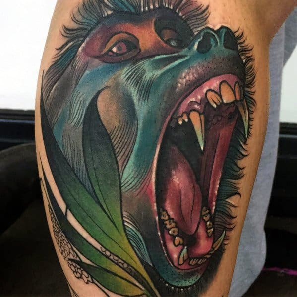 Realistic baboon tattoo with vivid colors, fierce open-mouthed expression, and detailed shading, featuring jungle leaves for a dynamic leg design.