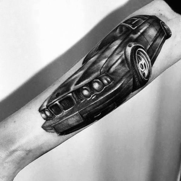 Realistic BMW tattoo on forearm, featuring a detailed front-angle view with bold shading and highlights for a dynamic 3D effect.