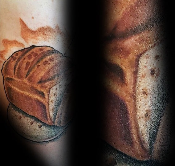Realistic tattoo of a golden brown loaf of bread with fine shading and texture, placed on a stone surface with a warm background for depth.