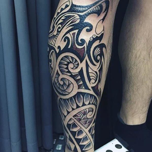 Bold tribal calf tattoo with intricate black ink patterns, swirling shapes, and geometric details for a striking and dynamic design