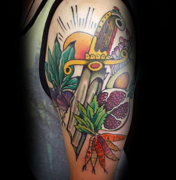 Vibrant sleeve tattoo featuring a dagger, carrots, berries, and leaves, blending bold colors and intricate shading for a dynamic and striking design.