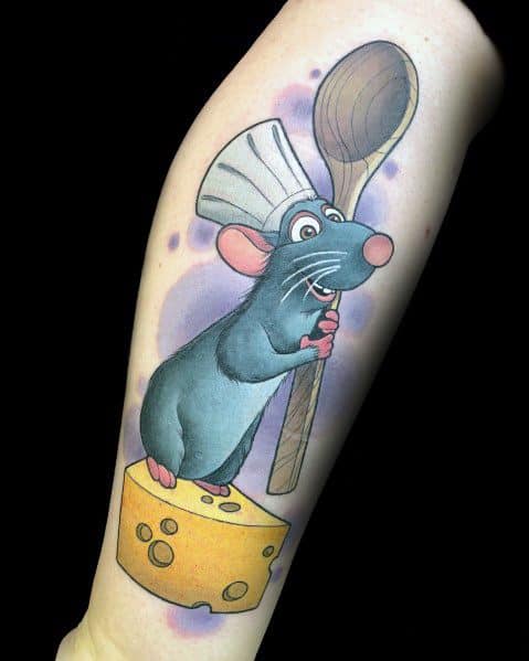 Colorful tattoo of a cartoon rat wearing a chef’s hat, holding a wooden spoon, and standing on a wedge of cheese, featuring smooth shading and vibrant details.