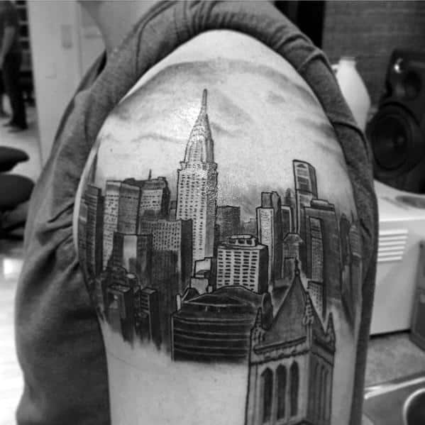 Black-and-grey Chrysler Building tattoo with a detailed New York City skyline, creating a bold urban-themed shoulder design.