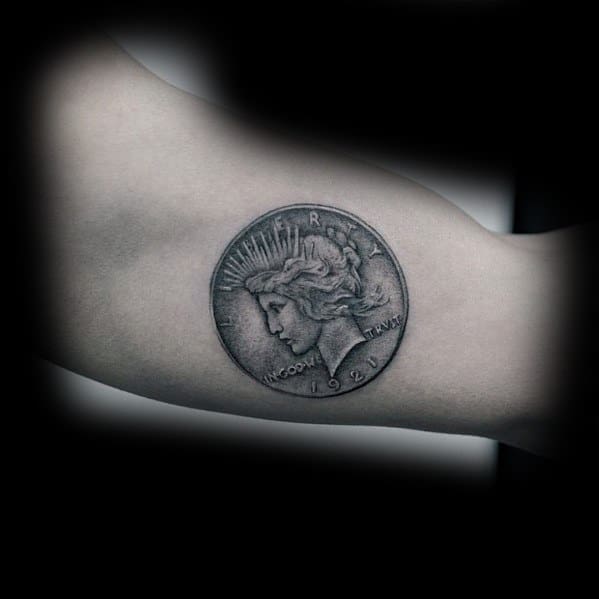 Realistic tattoo of a 1921 Peace Dollar coin on the inner arm, featuring intricate shading for a detailed and three-dimensional effect.