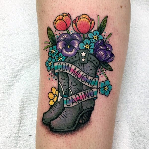 Colorful tattoo of a cowboy boot filled with vibrant flowers, featuring a banner reading "Con Mucho Cariño," symbolizing love, warmth, and Western charm.