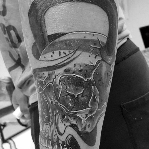 Realistic black and gray kettlebell skull tattoo with intricate shading and bold details, symbolizing strength, endurance, and a hardcore fitness mindset.