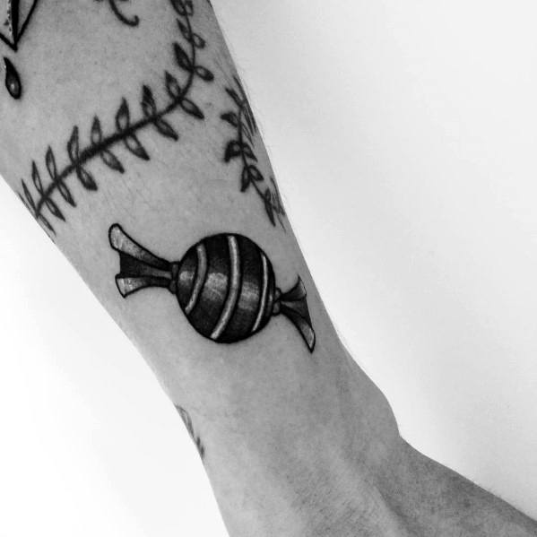 Black and grey wrapped candy tattoo with bold shading and fine line details, creating a classic and minimalist design on the forearm.