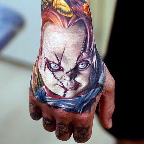 Realistic Chucky hand tattoo with piercing blue eyes, stitched face, and vivid colors, creating a bold and terrifying horror-inspired design.