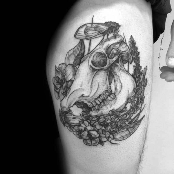 Detailed black and grey tattoo of a cow skull surrounded by flowers and a moth, blending natural and macabre elements on the upper arm.